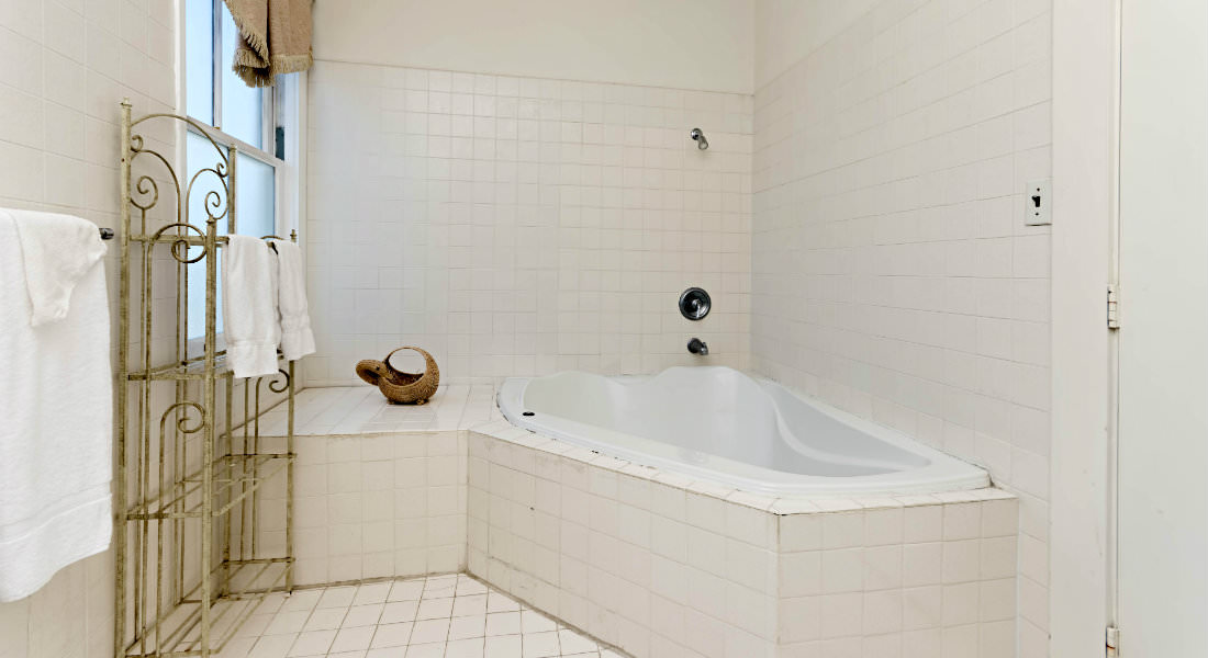 A whirlpool bathtub sets in the corner of the white bathroom