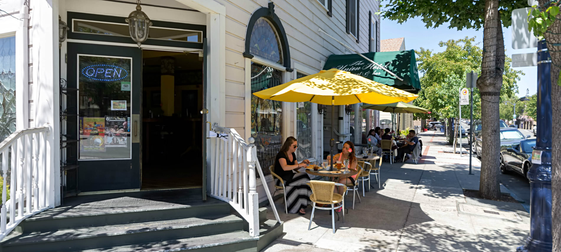 A view of an old building with rows of tables with yellow chairs and umbrellas along the sidewalk outside