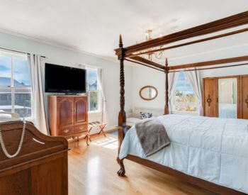 A bedroom with wood floors, light blue walls, a four poster canopy bed, a mirrored wardrobe, and a sitting area.