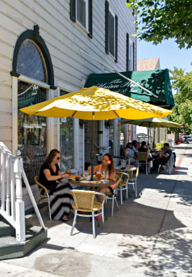 Rows of white and yellow tables and chairs with yellow umbrellas line the sidewalk outide the old building
